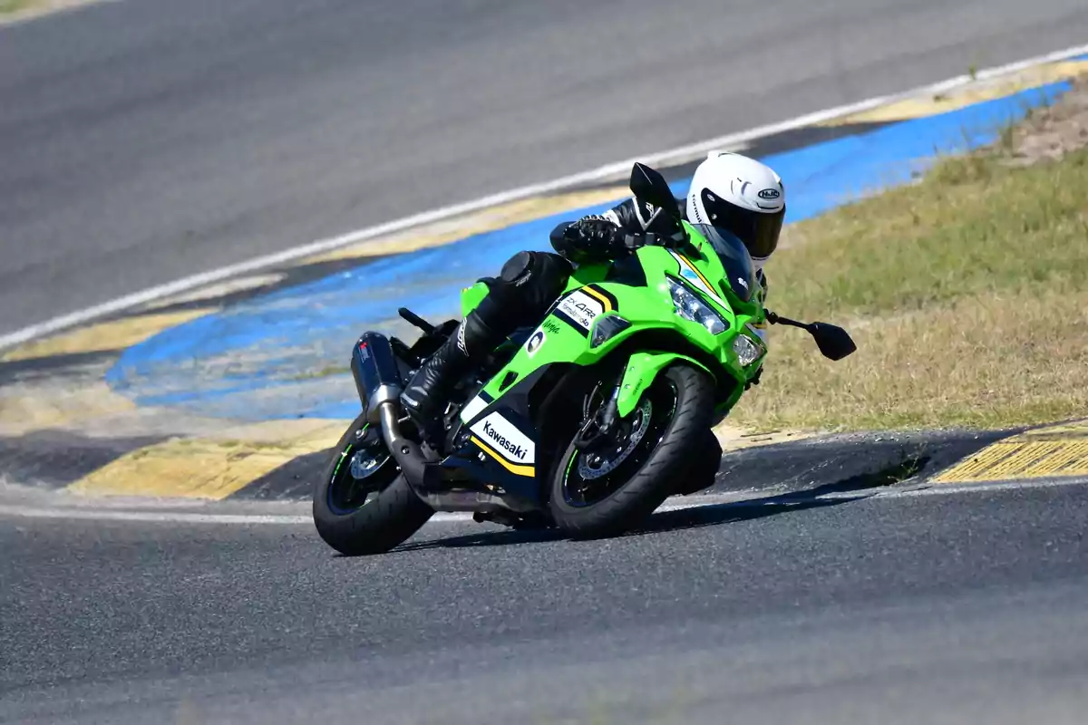 Motociclista con casco blanco conduciendo una moto deportiva verde Kawasaki en una curva de pista asfaltada Motociclista con casco blanco conduciendo una moto deportiva verde Kawasaki en una curva de pista asfaltada