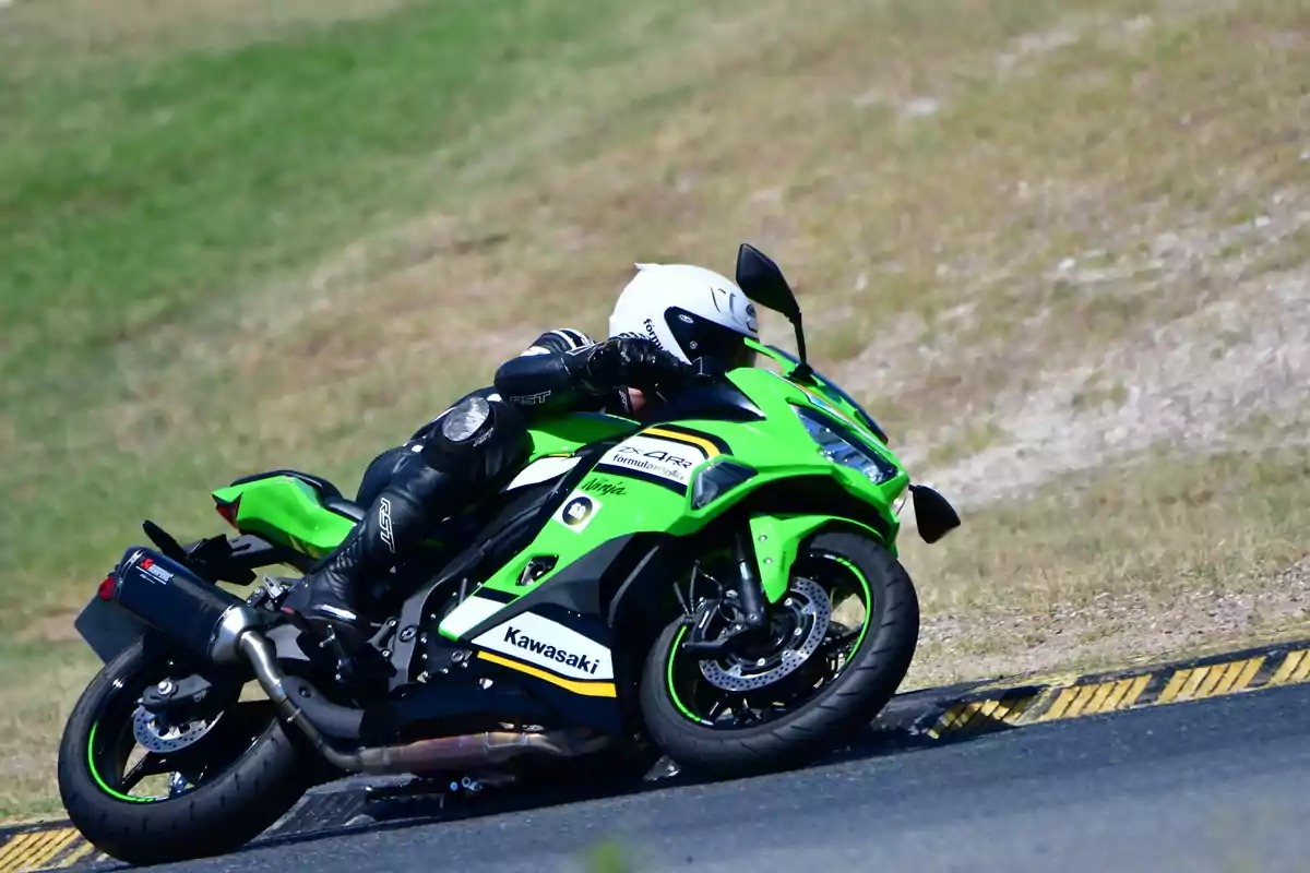 Motociclista con traje y casco de protección conduciendo una moto deportiva Kawasaki verde en una curva de pista asfaltada