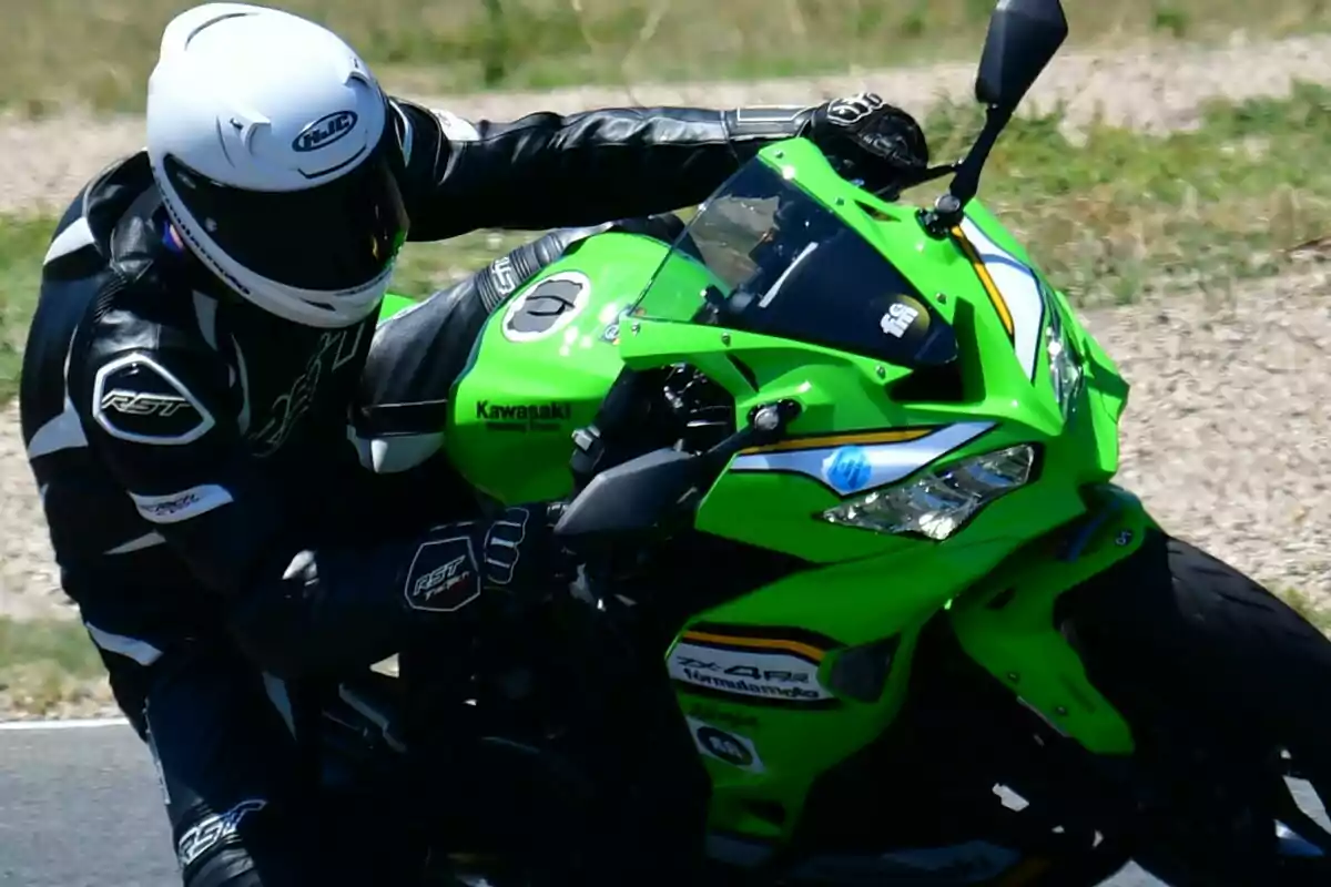 Persona con casco y traje de motociclista conduciendo una moto deportiva verde en una pista Persona con casco y traje de motociclista conduciendo una moto deportiva verde en una pista