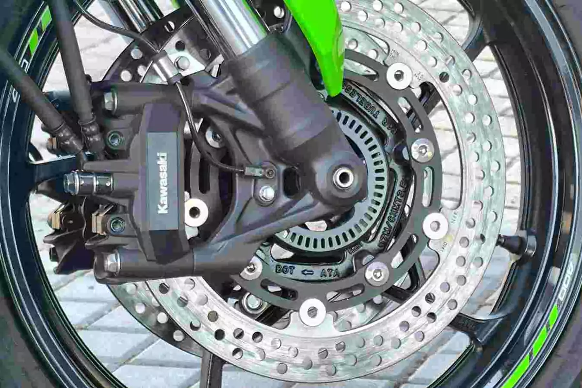 Detalle del freno de disco delantero de una motocicleta Kawasaki con pinza y sensor ABS visibles Detalle del freno de disco delantero de una motocicleta Kawasaki con pinza y sensor ABS visibles