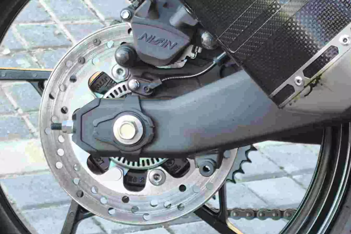 Detalle del freno de disco trasero de una motocicleta con caliper y cadena visibles Detalle del freno de disco trasero de una motocicleta con caliper y cadena visibles