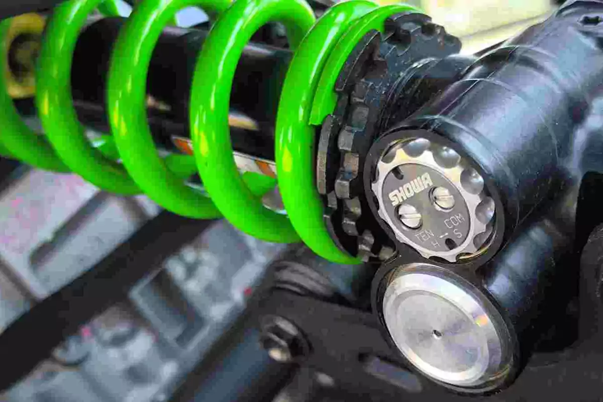 Detalle de un amortiguador de motocicleta con resorte verde y componentes metálicos Detalle de un amortiguador de motocicleta con resorte verde y componentes metálicos