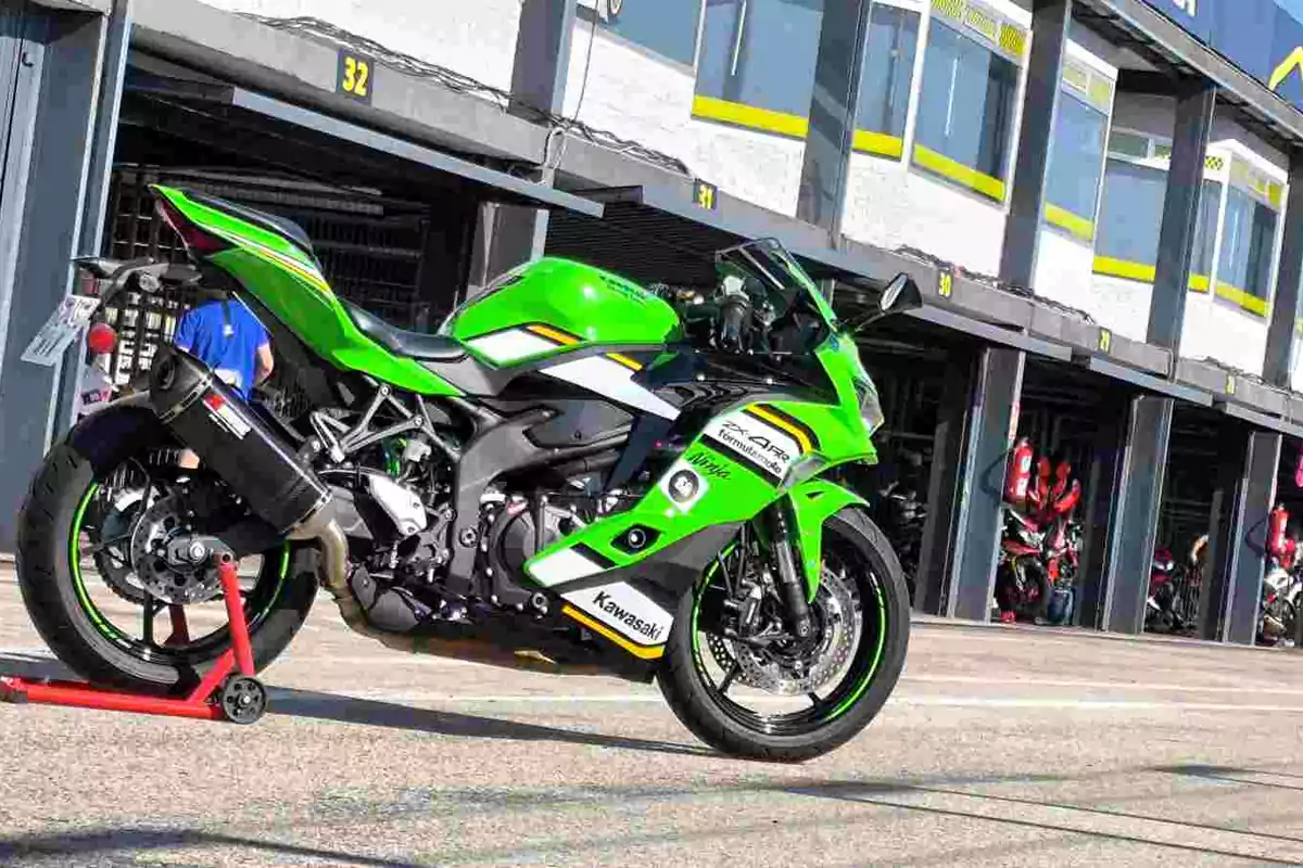 Motocicleta deportiva Kawasaki verde estacionada frente a boxes en un circuito de carreras Motocicleta deportiva Kawasaki verde estacionada frente a boxes en un circuito de carreras