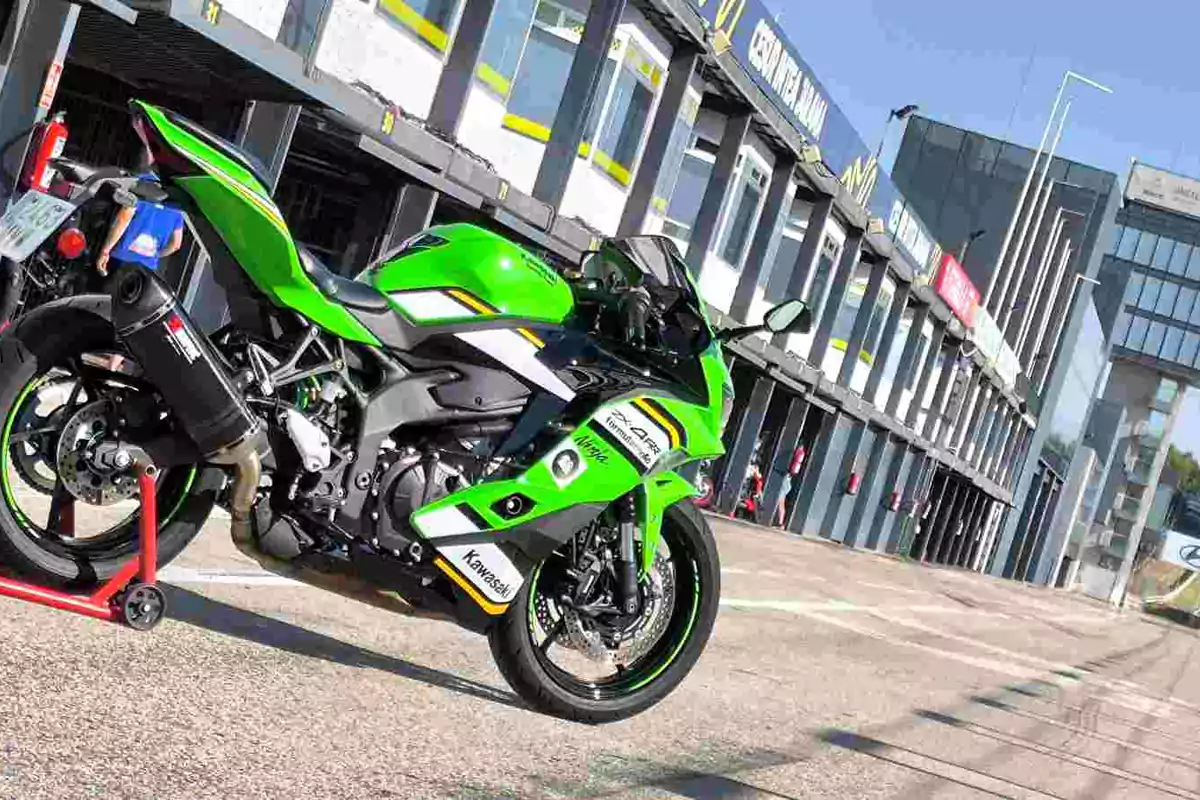 Motocicleta deportiva verde Kawasaki estacionada en un circuito de carreras frente a los boxes Motocicleta deportiva verde Kawasaki estacionada en un circuito de carreras frente a los boxes