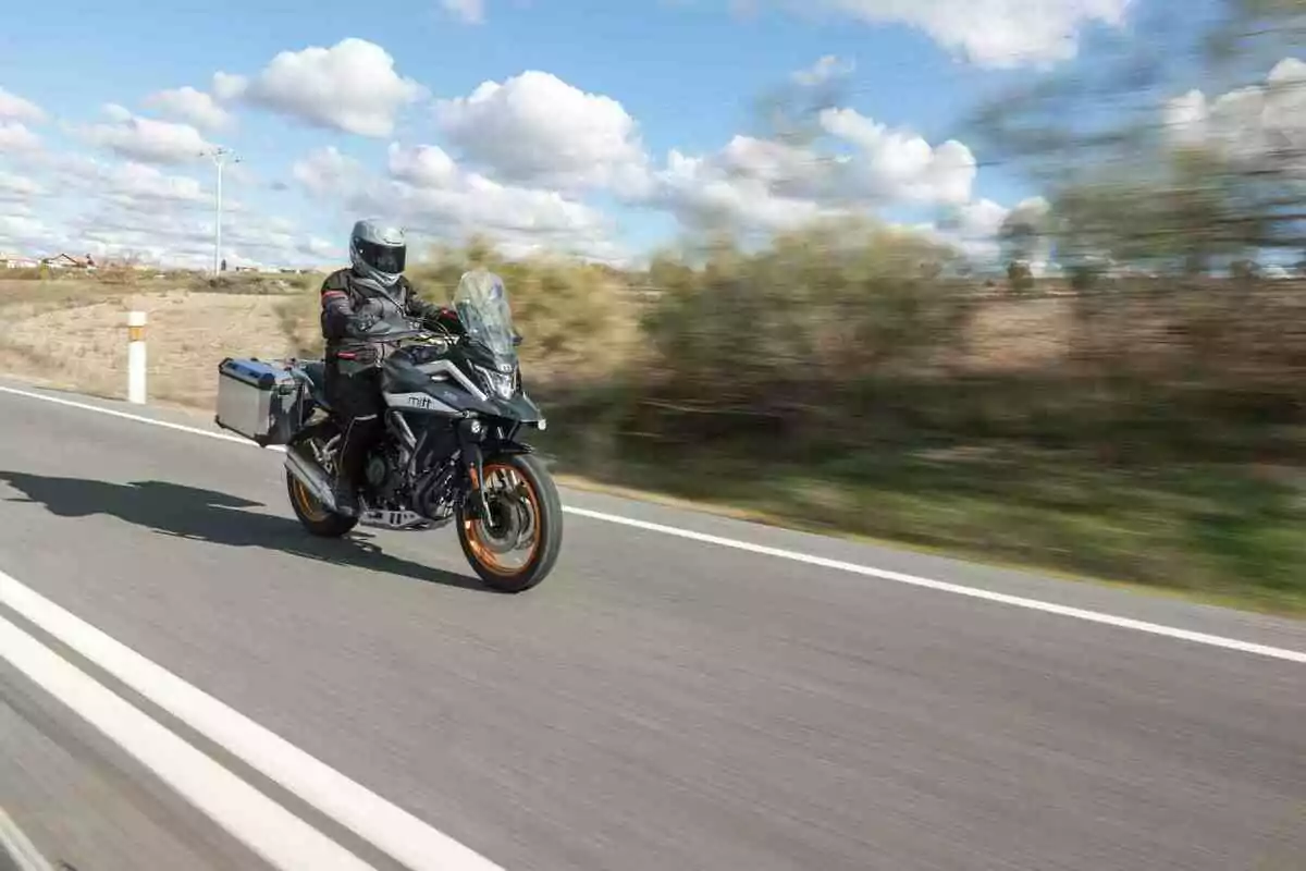 Persona conduciendo una motocicleta de turismo en una carretera con cielo azul y nubes al fondo Persona conduciendo una motocicleta de turismo en una carretera con cielo azul y nubes al fondo