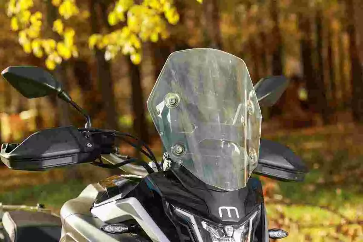 Motocicleta con parabrisas transparente en un entorno otoñal con árboles y hojas amarillas al fondo Motocicleta con parabrisas transparente en un entorno otoñal con árboles y hojas amarillas al fondo