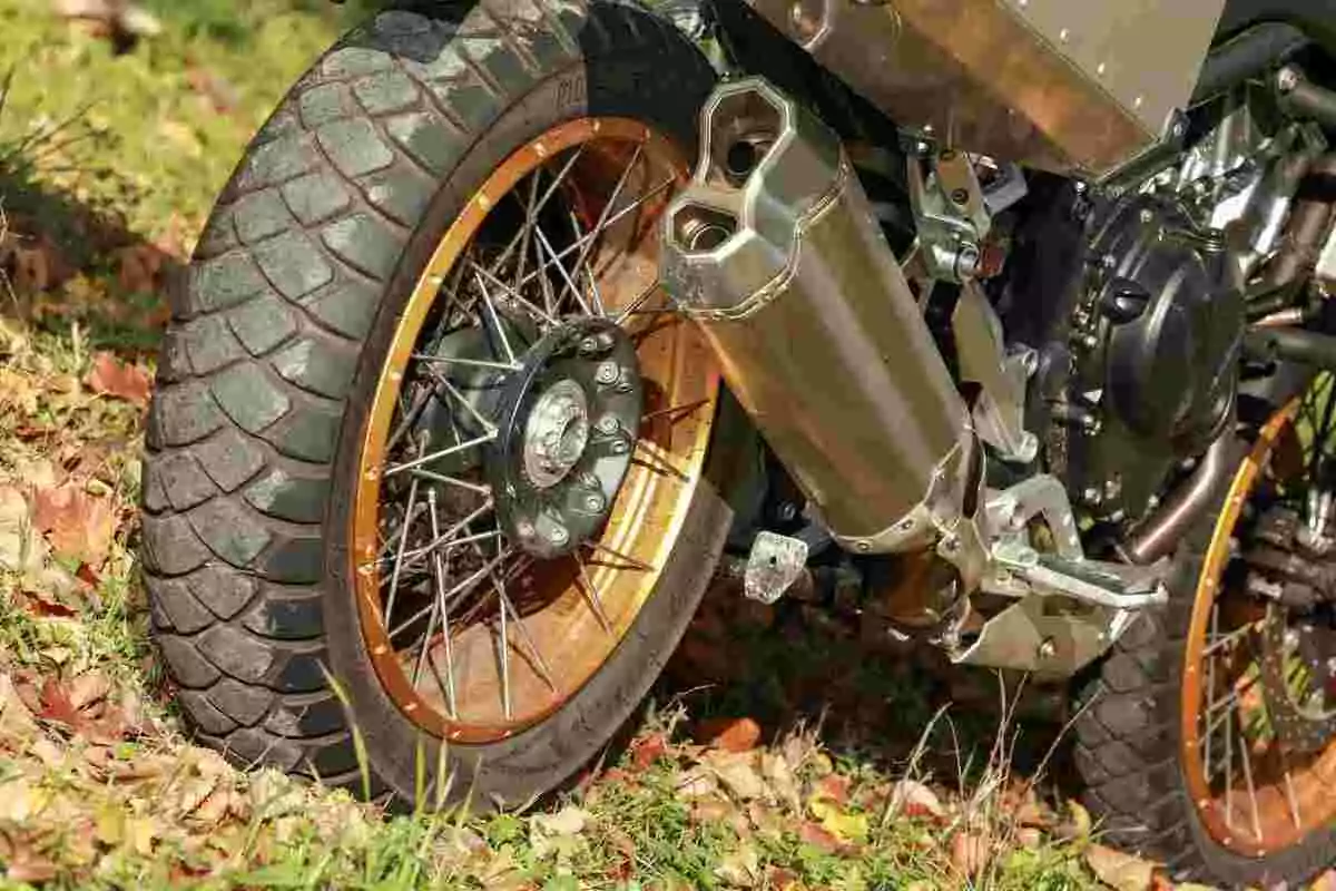 Rueda trasera de motocicleta con llanta de tacos y escape doble sobre césped y hojas secas Rueda trasera de motocicleta con llanta de tacos y escape doble sobre césped y hojas secas
