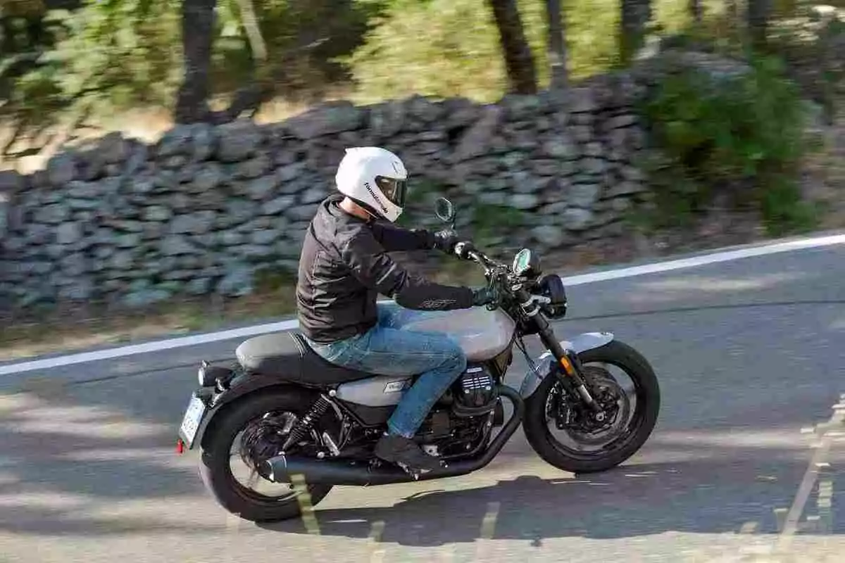 Persona conduciendo una motocicleta por una carretera rodeada de árboles y un muro de piedras Persona conduciendo una motocicleta por una carretera rodeada de árboles y un muro de piedras