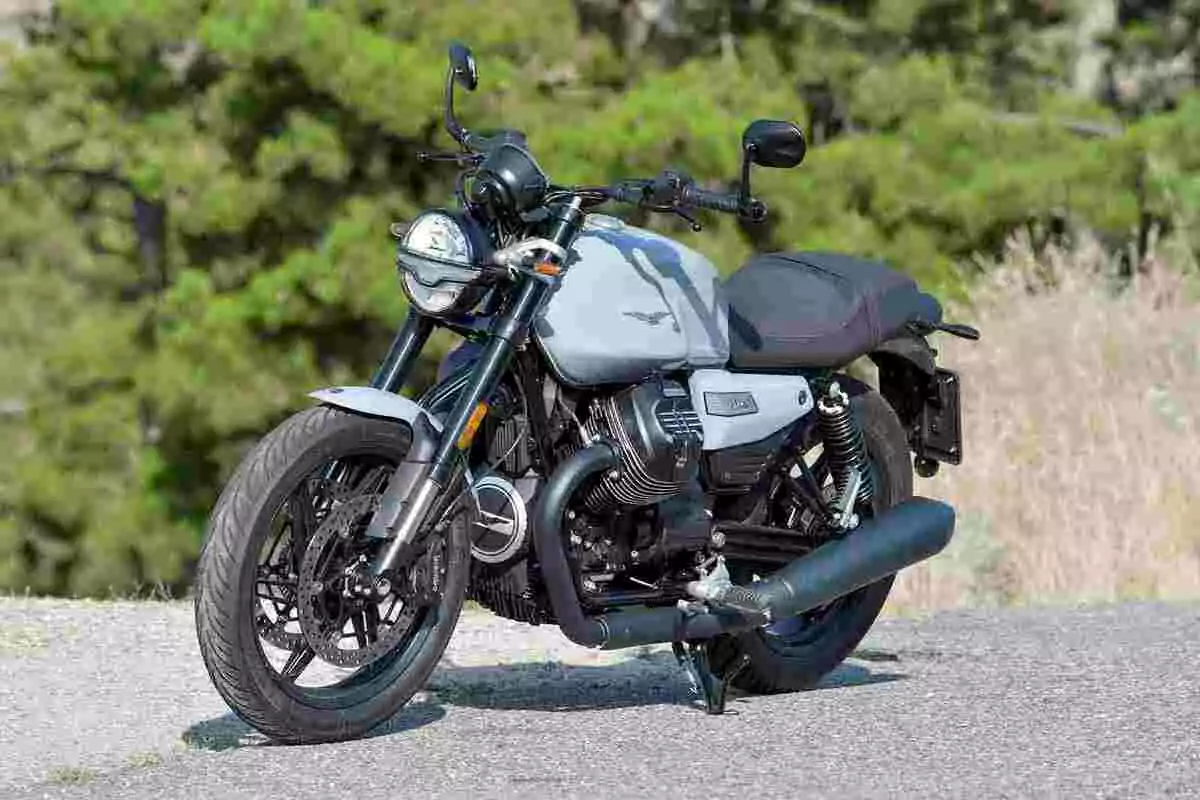 Motocicleta de estilo clásico estacionada sobre un camino asfaltado con árboles verdes al fondo Motocicleta de estilo clásico estacionada sobre un camino asfaltado con árboles verdes al fondo