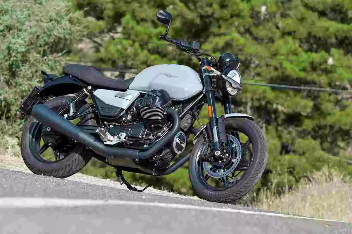 Motocicleta de estilo clásico estacionada en una carretera con árboles al fondo Motocicleta de estilo clásico estacionada en una carretera con árboles al fondo