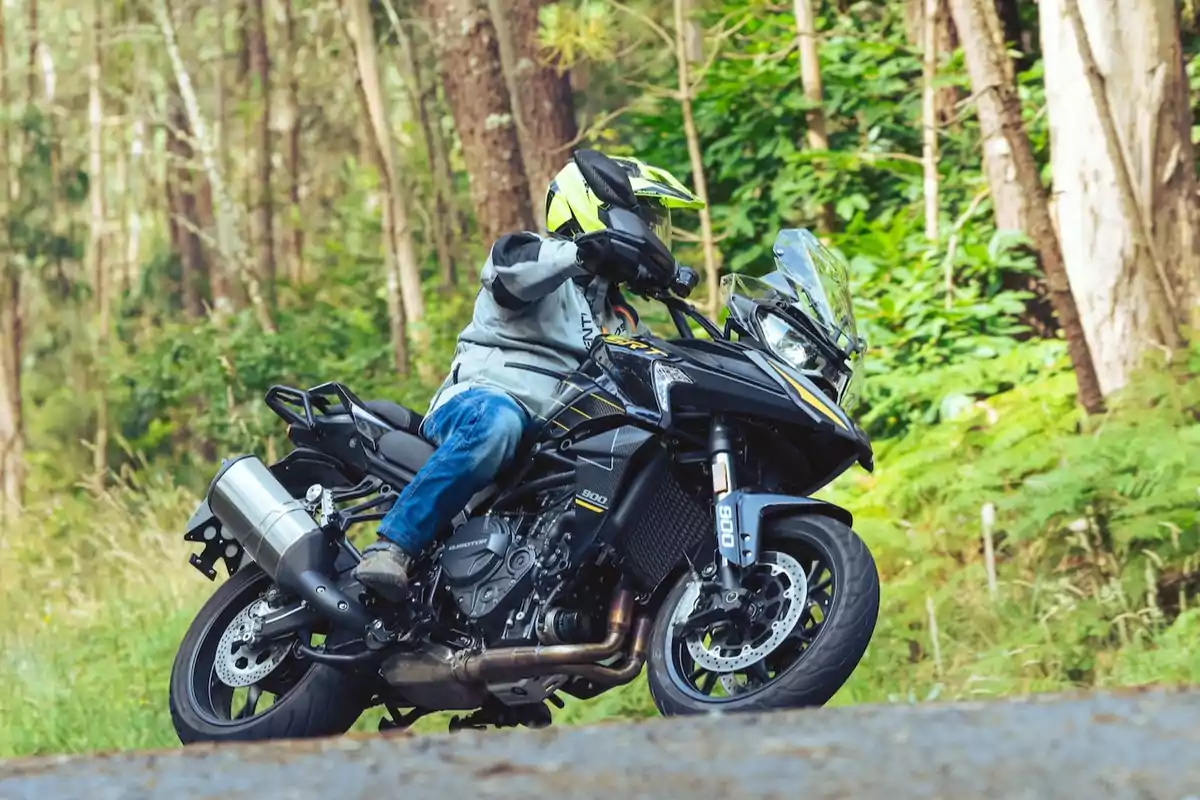 Persona conduint una motocicleta esportiva negra per una carretera envoltada d’arbres i vegetació Persona conduint una motocicleta esportiva negra per una carretera envoltada d’arbres i vegetació
