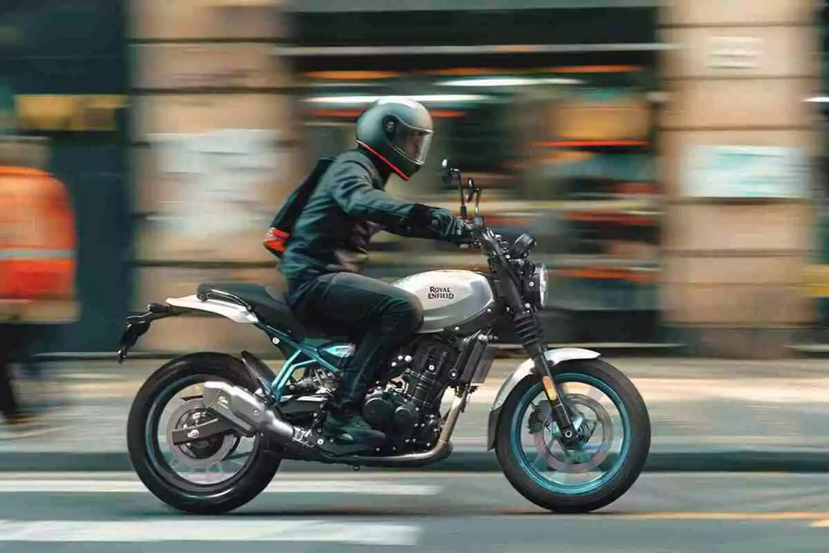 Persona con casco negro conduciendo una motocicleta Royal Enfield plateada por una calle urbana con fondo desenfocado Persona con casco negro conduciendo una motocicleta Royal Enfield plateada por una calle urbana con fondo desenfocado