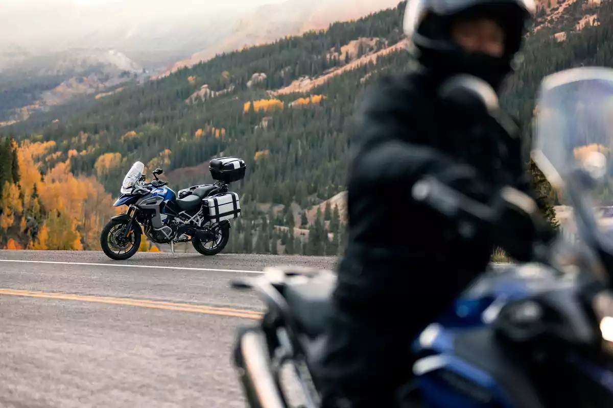 Motorcycle parked on a mountain road with a landscape of trees and mountains in the background and a blurred motorcyclist in the foreground Motorcycle parked on a mountain road with a landscape of trees and mountains in the background and a blurred motorcyclist in the foreground