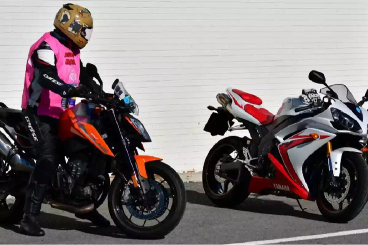Person wearing a helmet and a pink vest riding an orange motorcycle next to a white and red sports motorcycle parked in front of a white wall Person wearing a helmet and a pink vest riding an orange motorcycle next to a white and red sports motorcycle parked in front of a white wall