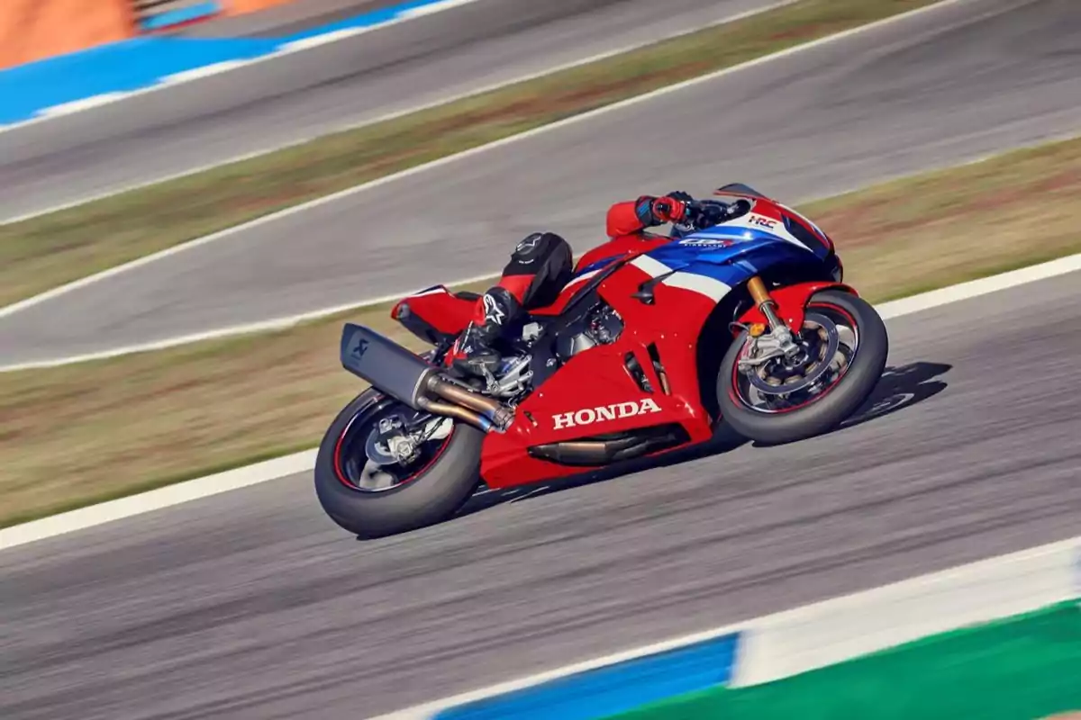 Motociclista con traje negro y rojo conduciendo una motocicleta deportiva Honda roja en una pista de carreras Motociclista con traje negro y rojo conduciendo una motocicleta deportiva Honda roja en una pista de carreras