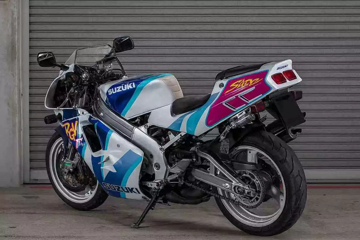 Motocicleta deportiva Suzuki de colores blanco, azul y morado estacionada frente a una puerta metálica enrollable Motocicleta deportiva Suzuki de colores blanco, azul y morado estacionada frente a una puerta metálica enrollable