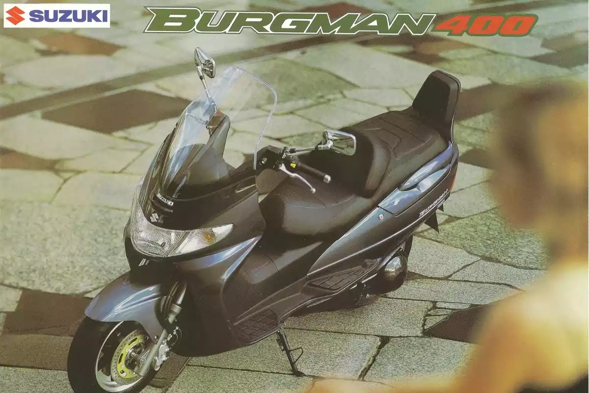 Motocicleta Suzuki Burgman 400 estacionada sobre un pavimento de piedra con el logo de Suzuki en la esquina superior izquierda Motocicleta Suzuki Burgman 400 estacionada sobre un pavimento de piedra con el logo de Suzuki en la esquina superior izquierda