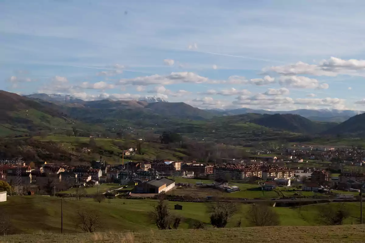 Vista panorámica de un pueblo rodeado de montañas verdes bajo un cielo azul con nubes dispersas Vista panorámica de un pueblo rodeado de montañas verdes bajo un cielo azul con nubes dispersas