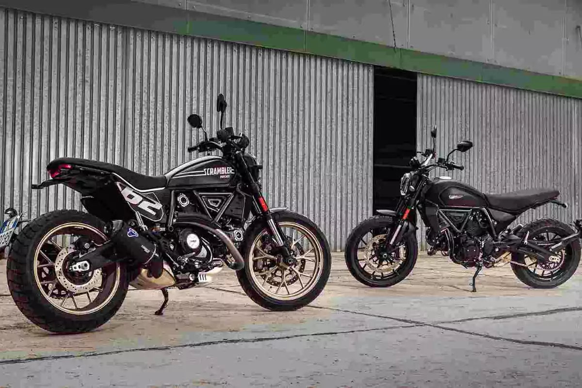 Dos motocicletas tipo scrambler estacionadas frente a una pared metálica ondulada Dos motocicletas tipo scrambler estacionadas frente a una pared metálica ondulada