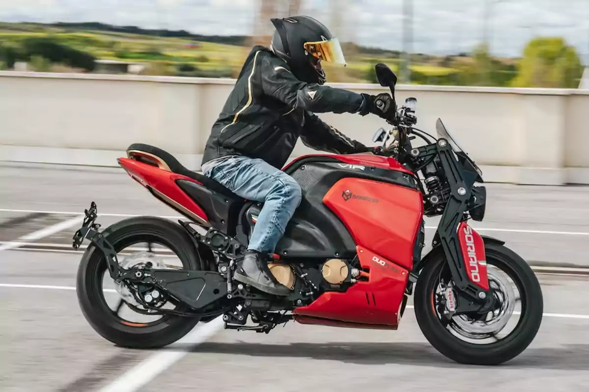 Persona conduciendo una motocicleta eléctrica roja en una carretera, usando casco y chaqueta de protección Persona conduciendo una motocicleta eléctrica roja en una carretera, usando casco y chaqueta de protección