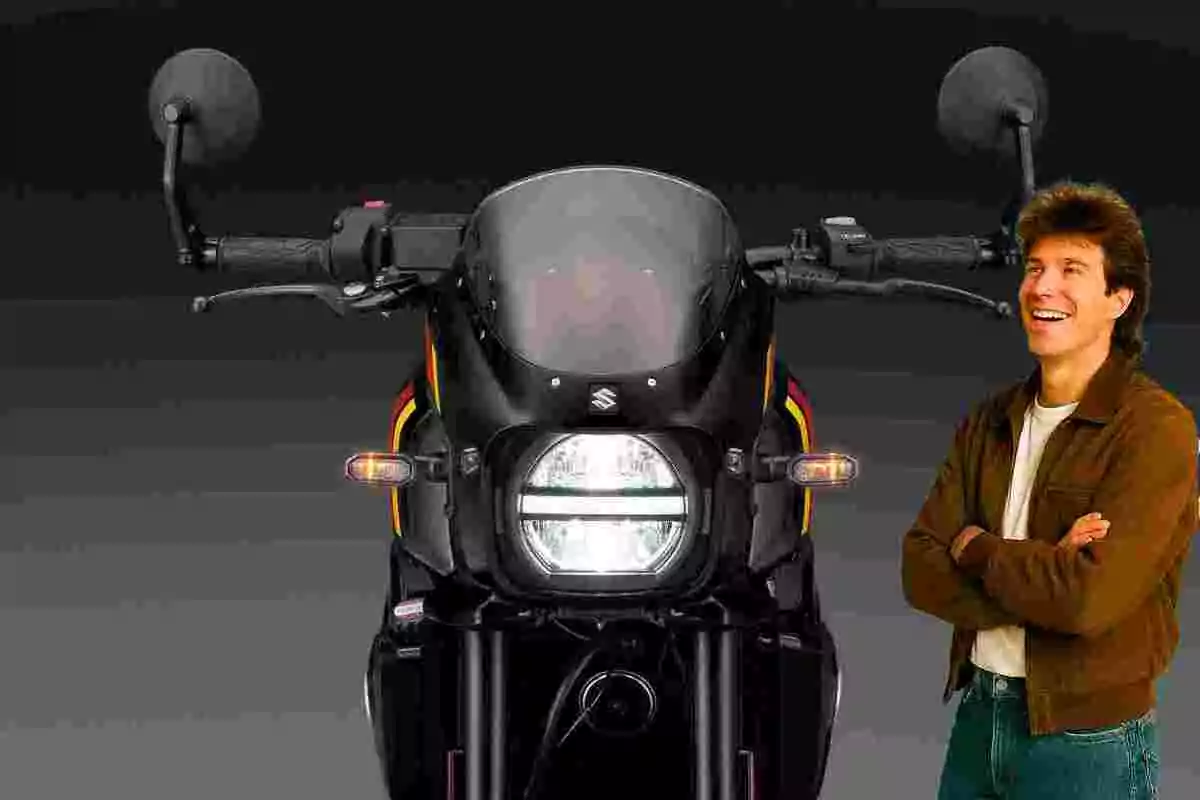Hombre sonriente de pie junto a una motocicleta negra vista de frente sobre fondo oscuro