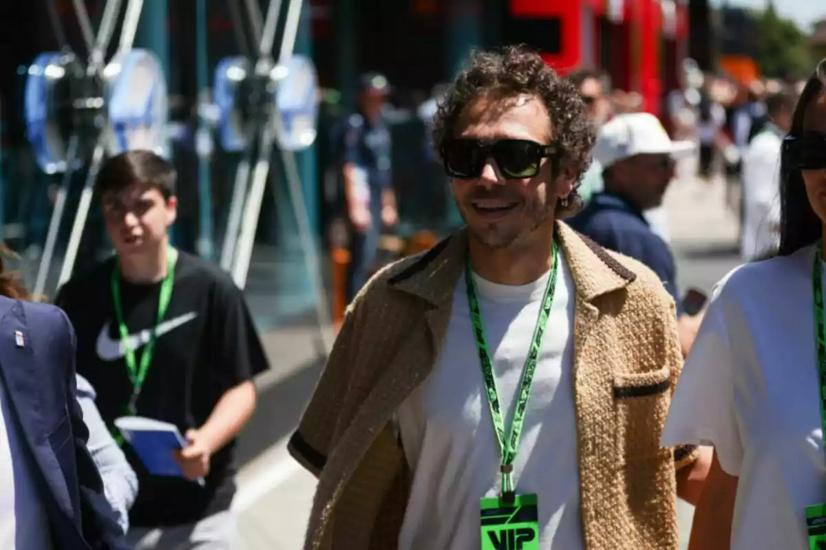 Hombre con gafas de sol y gafete VIP verde caminando al aire libre entre una multitud en un evento deportivo Hombre con gafas de sol y gafete VIP verde caminando al aire libre entre una multitud en un evento deportivo