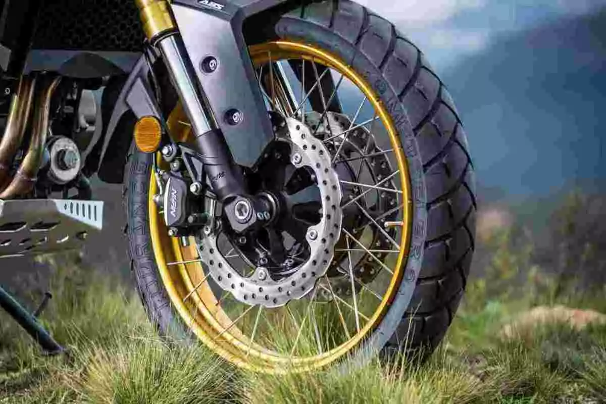 Llanta delantera de motocicleta con rines dorados y freno de disco sobre pasto Llanta delantera de motocicleta con rines dorados y freno de disco sobre pasto