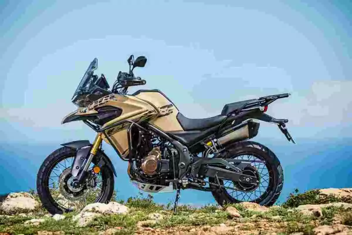 Motocicleta tipo adventure color dorado estacionada sobre terreno rocoso con el cielo azul de fondo Motocicleta tipo adventure color dorado estacionada sobre terreno rocoso con el cielo azul de fondo