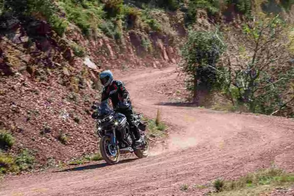 Persona conduciendo una motocicleta en un camino de terracería rodeado de vegetación y colinas Persona conduciendo una motocicleta en un camino de terracería rodeado de vegetación y colinas