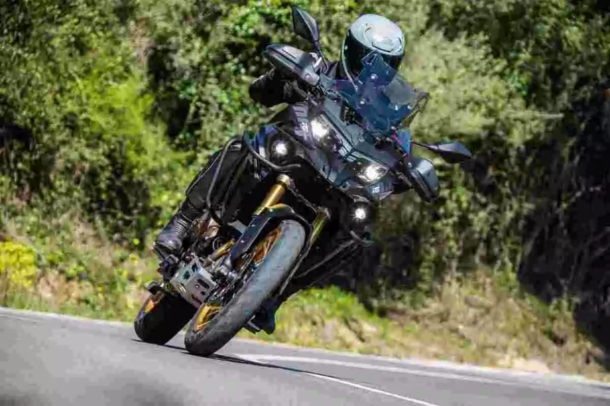 Motociclista con casco conduciendo una moto deportiva negra en una carretera rodeada de vegetación Motociclista con casco conduciendo una moto deportiva negra en una carretera rodeada de vegetación
