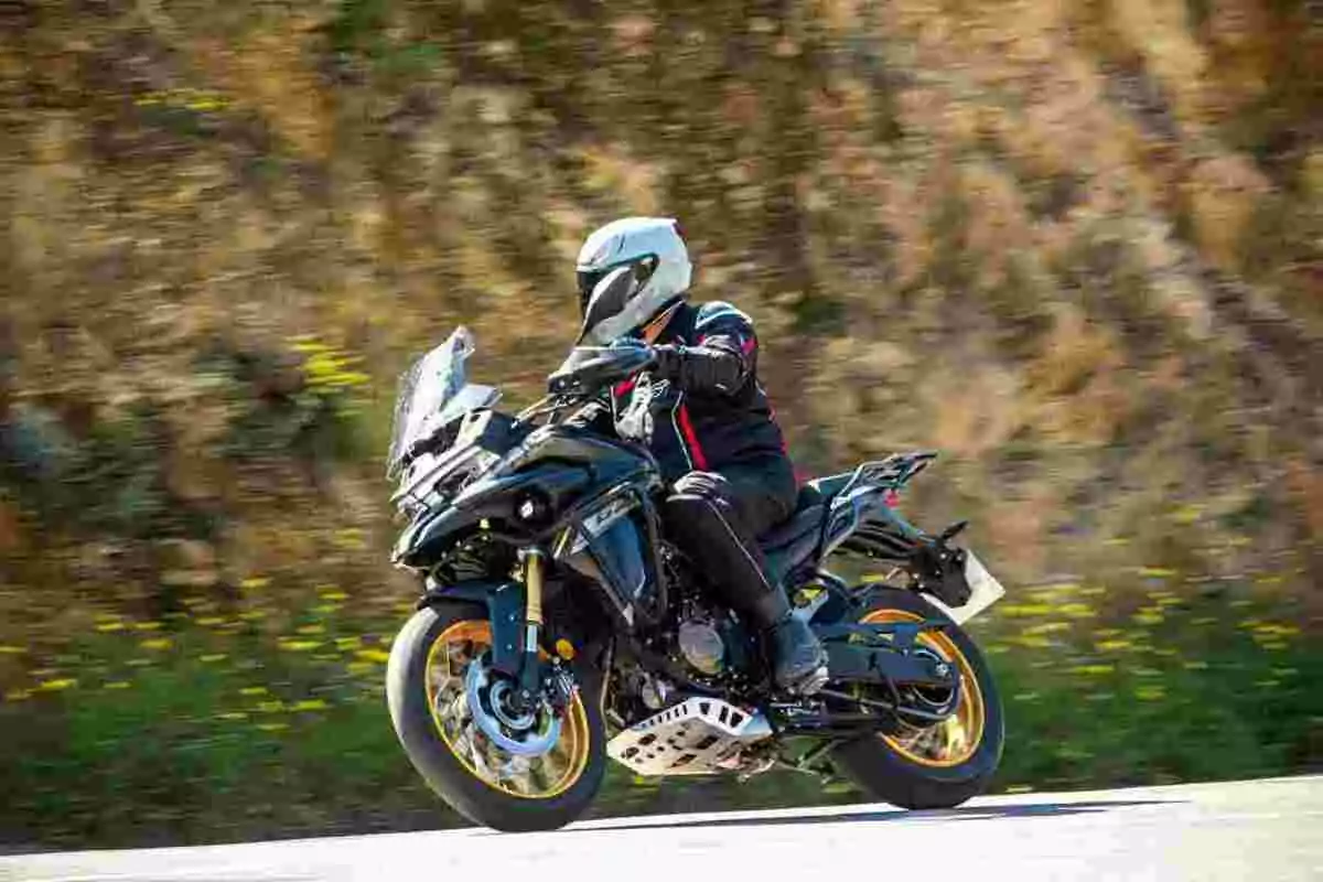 Persona con casco y chaqueta negra conduciendo una motocicleta deportiva en una carretera junto a un paisaje natural desenfocado