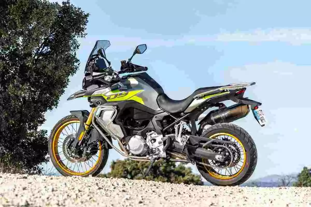 Motocicleta d’aventura estacionada sobre un camí de terra amb un fons de cel blau i vegetació a un costat Motocicleta d’aventura estacionada sobre un camí de terra amb un fons de cel blau i vegetació a un costat
