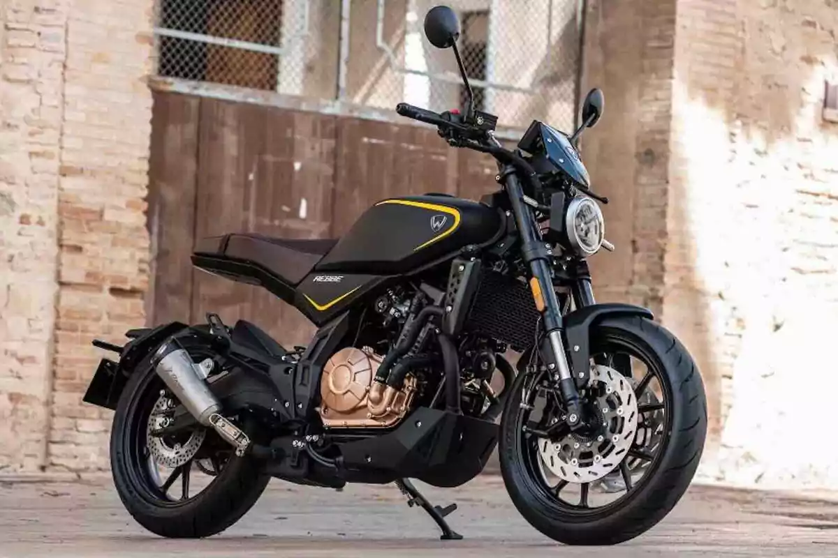 Motocicleta negra con detalles dorados estacionada sobre un suelo de piedra frente a una pared de ladrillo Motocicleta negra con detalles dorados estacionada sobre un suelo de piedra frente a una pared de ladrillo