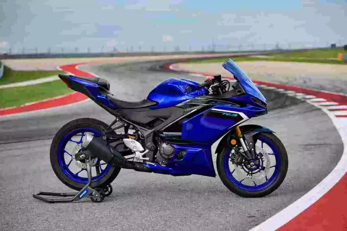 Motocicleta deportiva azul estacionada sobre una pista de carreras asfaltada con curvas y césped al fondo Motocicleta deportiva azul estacionada sobre una pista de carreras asfaltada con curvas y césped al fondo