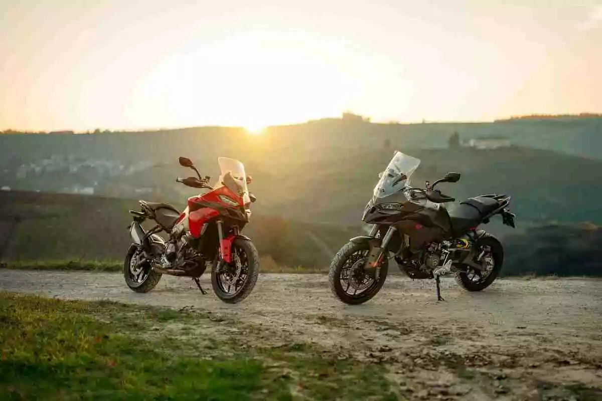 Dos motocicletas estacionadas en un camino de tierra con un paisaje de colinas al fondo y el sol poniéndose en el horizonte Dos motocicletas estacionadas en un camino de tierra con un paisaje de colinas al fondo y el sol poniéndose en el horizonte