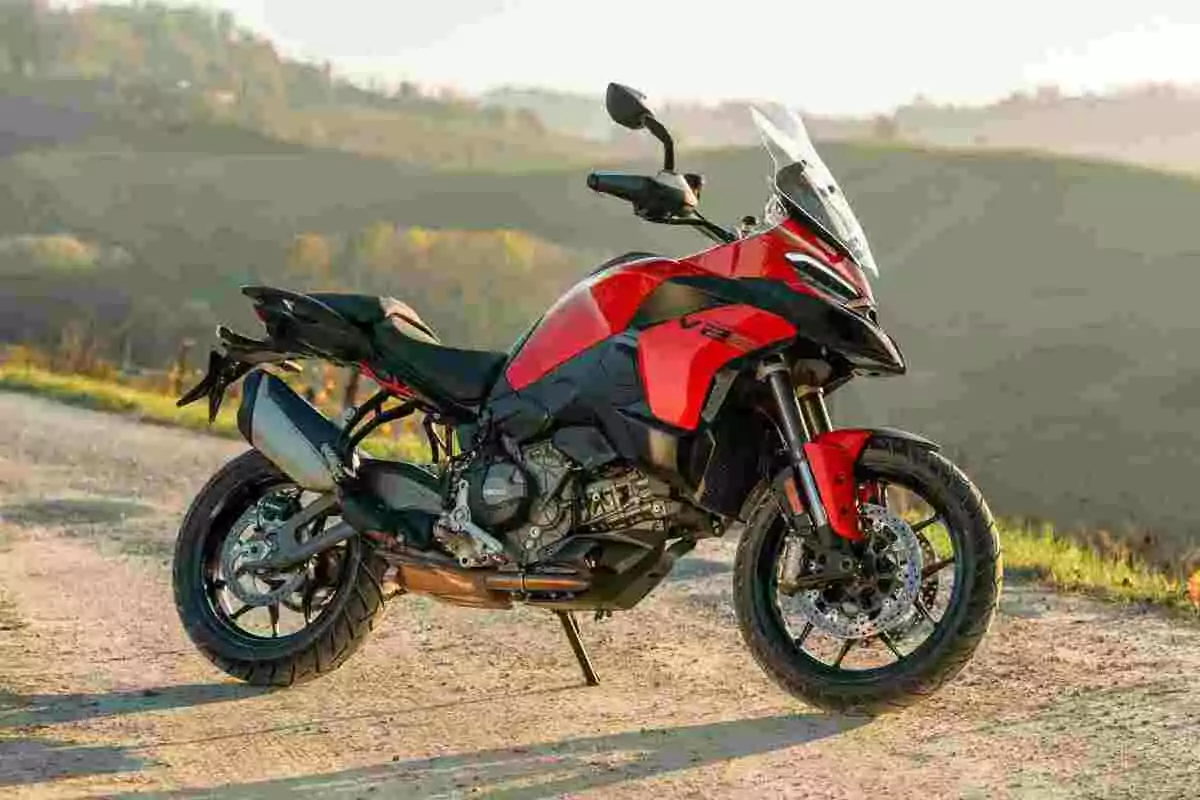 Motocicleta deportiva roja y negra estacionada en un camino de tierra con paisaje de colinas al fondo Motocicleta deportiva roja y negra estacionada en un camino de tierra con paisaje de colinas al fondo