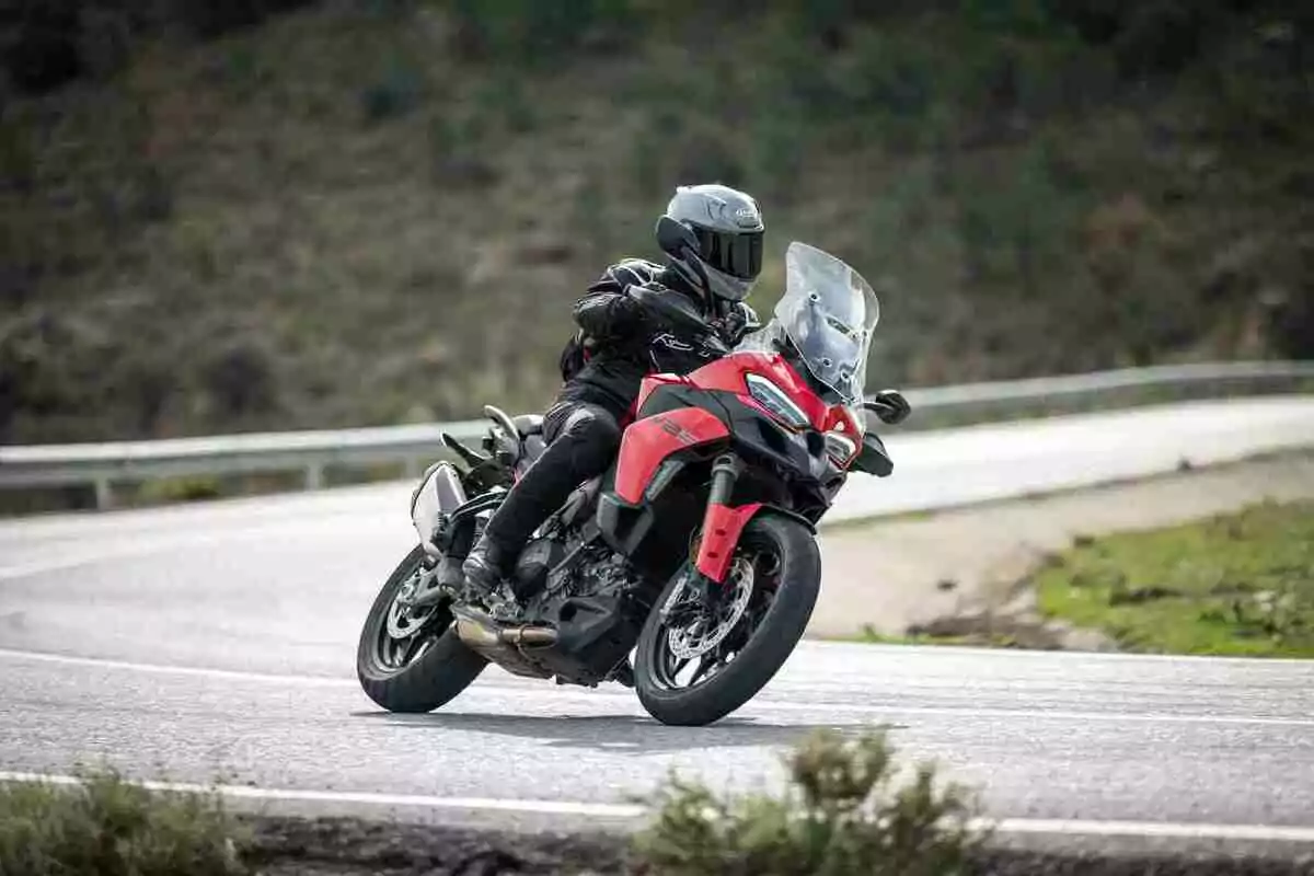 Persona con casco y equipo de protección conduciendo una motocicleta roja en una carretera curva rodeada de vegetación