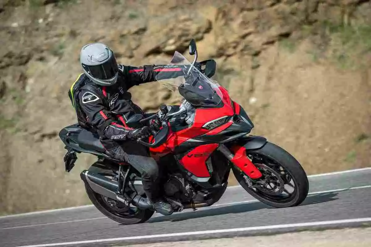 Persona conduciendo una motocicleta deportiva roja en una carretera asfaltada junto a una ladera de tierra Persona conduciendo una motocicleta deportiva roja en una carretera asfaltada junto a una ladera de tierra
