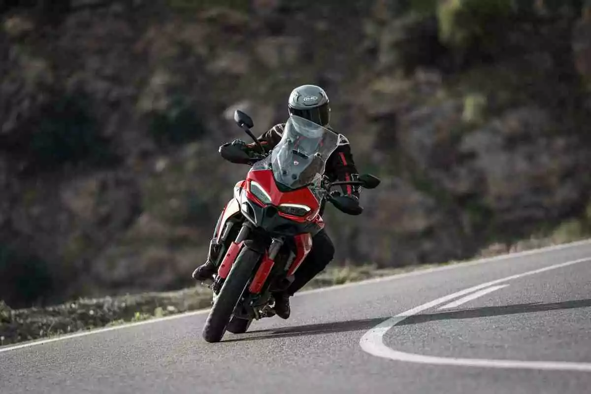 Persona conduciendo una motocicleta roja en una carretera curvada rodeada de paisaje montañoso Persona conduciendo una motocicleta roja en una carretera curvada rodeada de paisaje montañoso