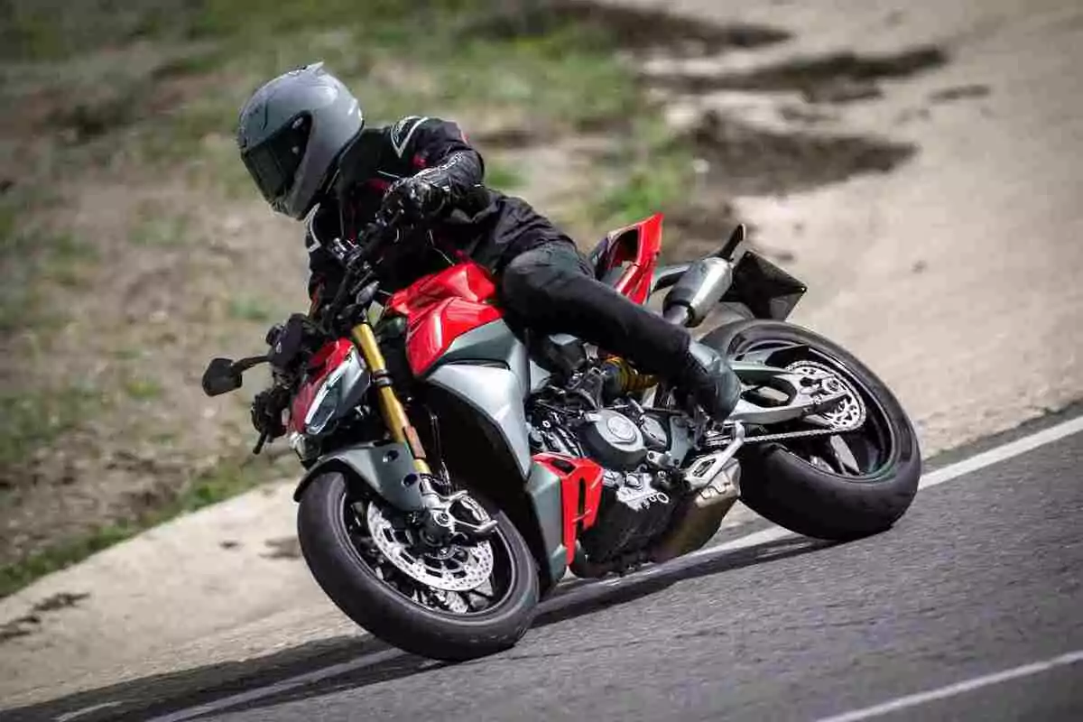 Persona con casco y equipo de protección conduciendo una motocicleta deportiva roja en una curva de carretera Persona con casco y equipo de protección conduciendo una motocicleta deportiva roja en una curva de carretera
