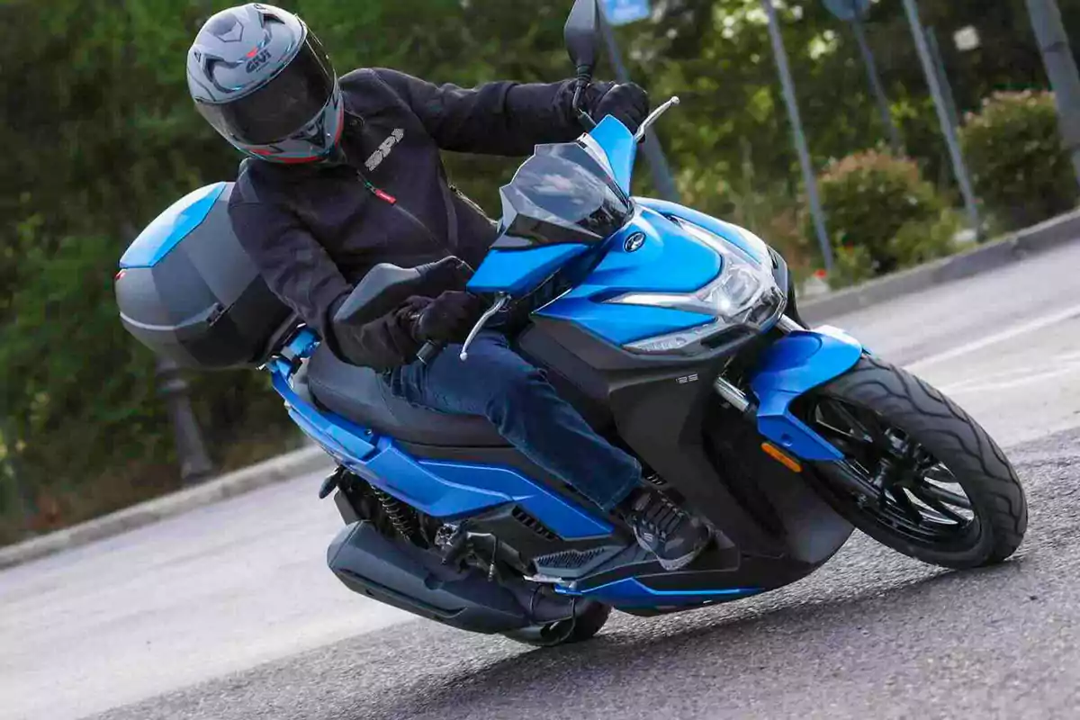Persona conduciendo una moto scooter azul en una curva sobre asfalto Persona conduciendo una moto scooter azul en una curva sobre asfalto