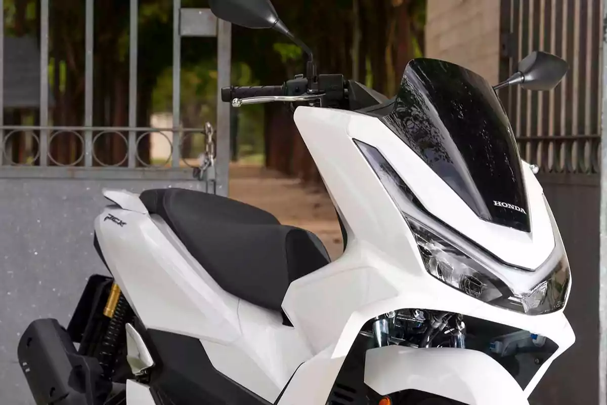 Motocicleta tipo scooter Honda blanca estacionada frente a un portón metálico Motocicleta tipo scooter Honda blanca estacionada frente a un portón metálico
