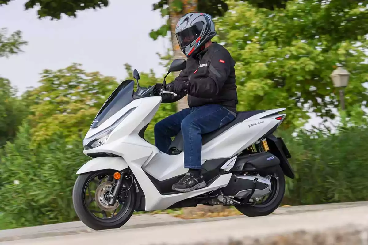 Persona conduciendo una motocicleta blanca en una carretera rodeada de vegetación Persona conduciendo una motocicleta blanca en una carretera rodeada de vegetación