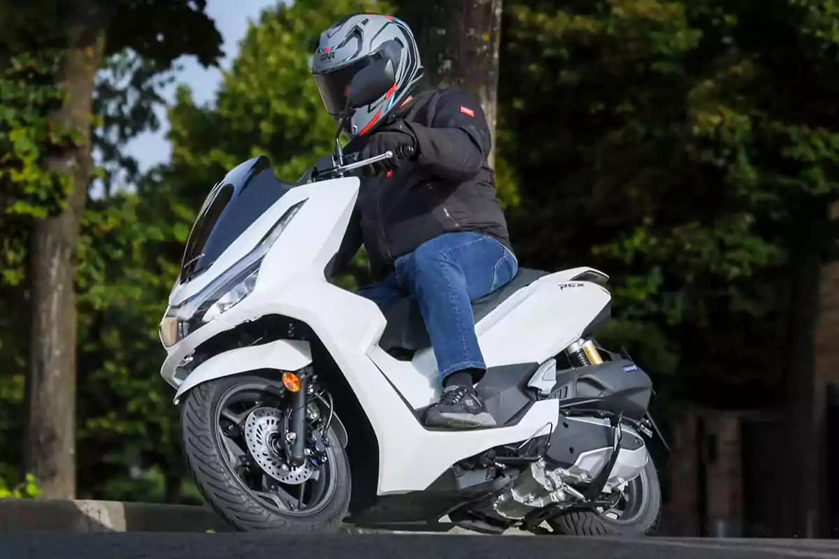 Persona conduciendo una motocicleta tipo scooter blanca en una calle rodeada de árboles Persona conduciendo una motocicleta tipo scooter blanca en una calle rodeada de árboles