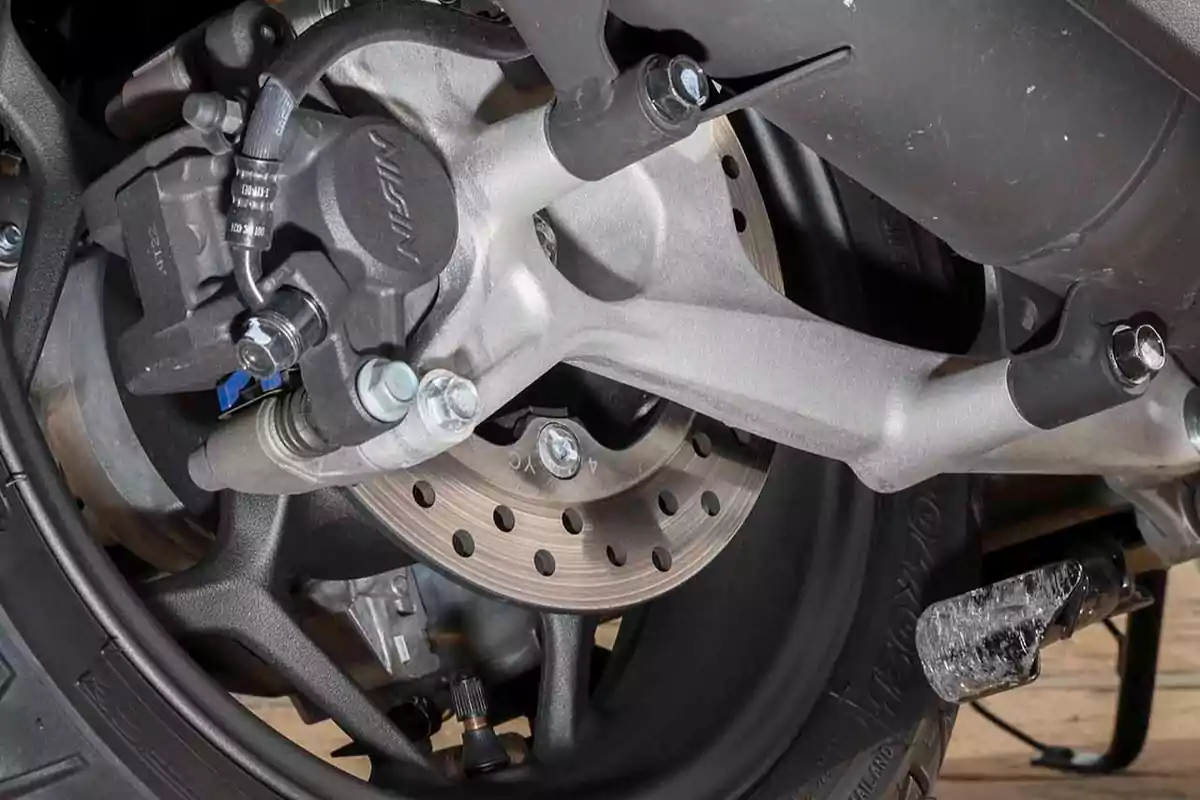 Detalle de un freno de disco trasero de motocicleta con cáliper y componentes metálicos visibles Detalle de un freno de disco trasero de motocicleta con cáliper y componentes metálicos visibles
