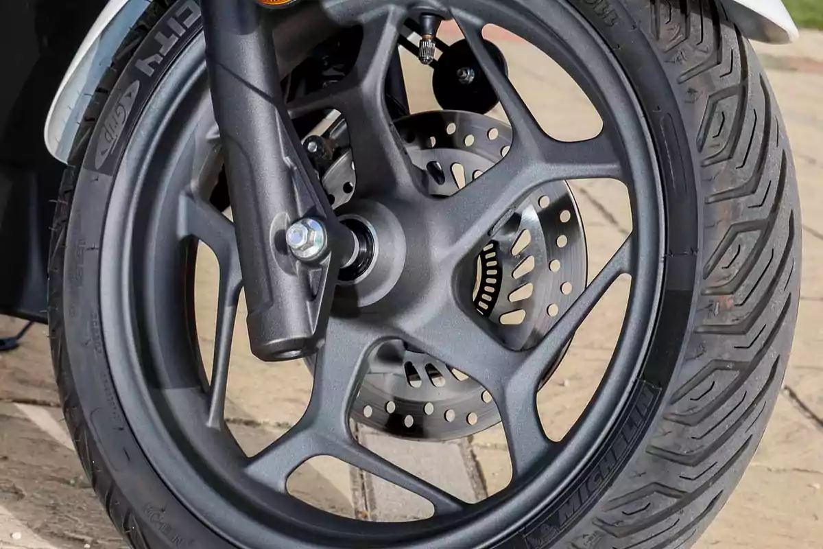 Llanta delantera de motocicleta con freno de disco y neumático Michelin sobre pavimento Llanta delantera de motocicleta con freno de disco y neumático Michelin sobre pavimento