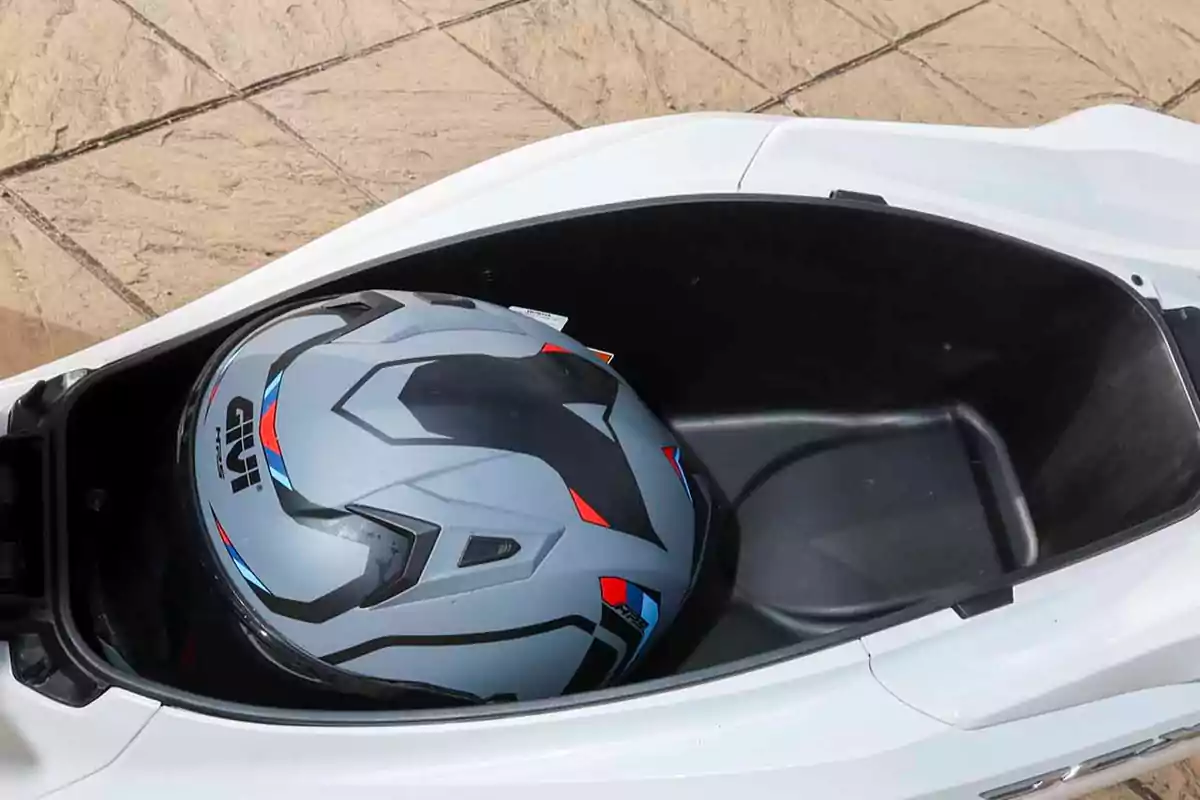 Casco de motocicleta guardado en el compartimiento debajo del asiento de una moto blanca Casco de motocicleta guardado en el compartimiento debajo del asiento de una moto blanca