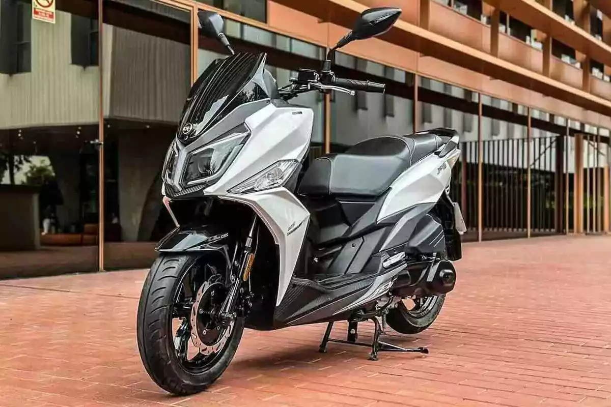 Motocicleta tipo scooter color blanco estacionada sobre un piso de ladrillo frente a un edificio moderno Motocicleta tipo scooter color blanco estacionada sobre un piso de ladrillo frente a un edificio moderno
