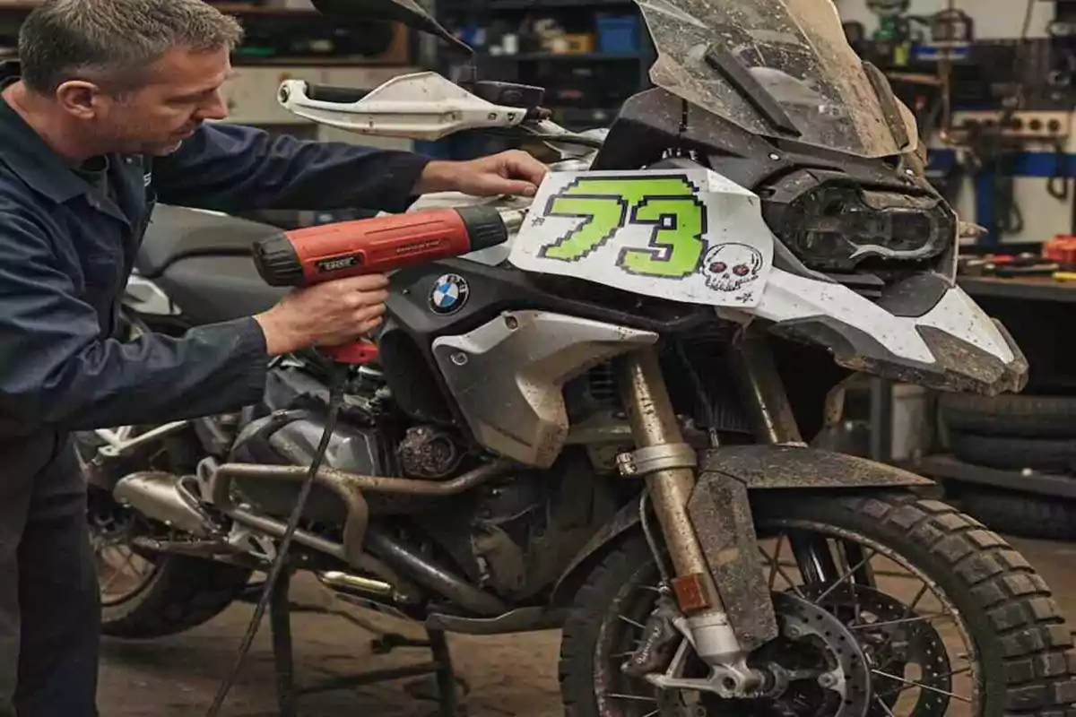 Hombre aplicando un vinil con el número 73 y una calavera en una motocicleta BMW sucia dentro de un taller Hombre aplicando un vinil con el número 73 y una calavera en una motocicleta BMW sucia dentro de un taller