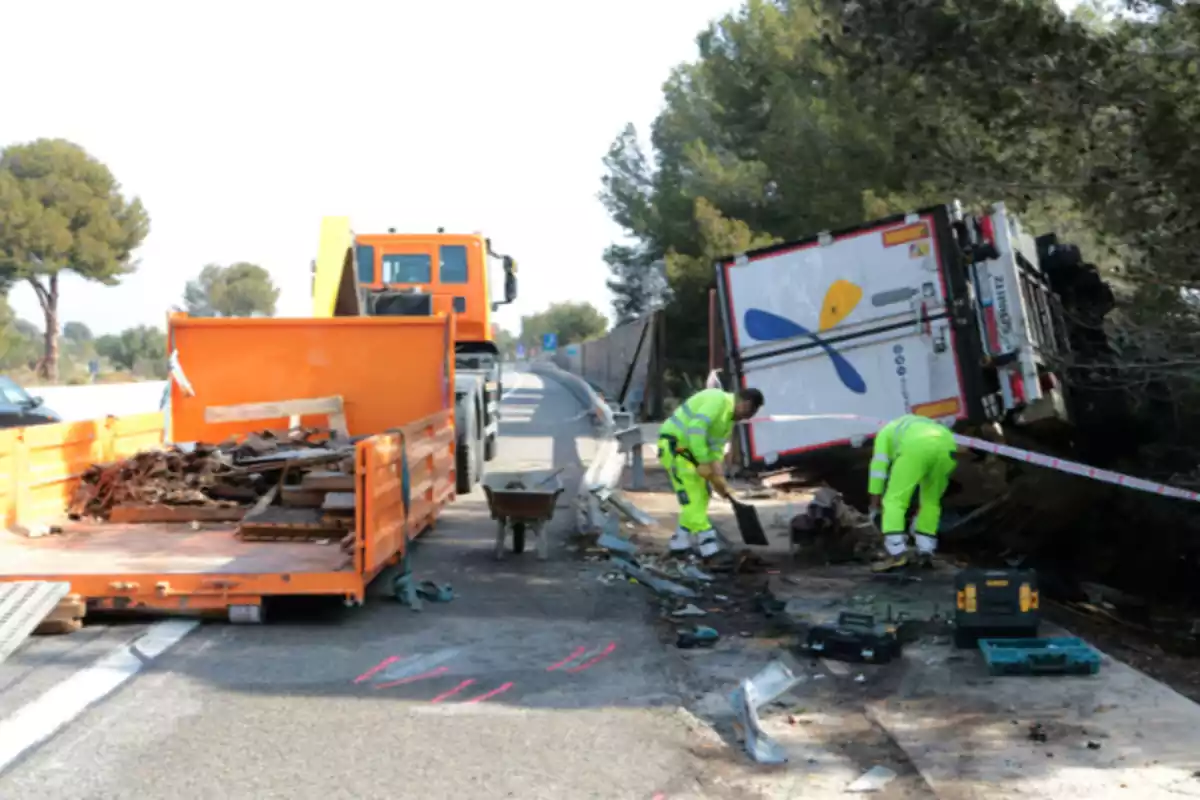 Imagen del punto de la AP-7, en el Vendrell (Tarragona), en la que aparece un camión volcado fuera de la vía y dos personas haciendo su trabajo el día posterior al accidente Imagen del punto de la AP-7, en el Vendrell (Tarragona), en la que aparece un camión volcado fuera de la vía y dos personas haciendo su trabajo el día posterior al accidente
